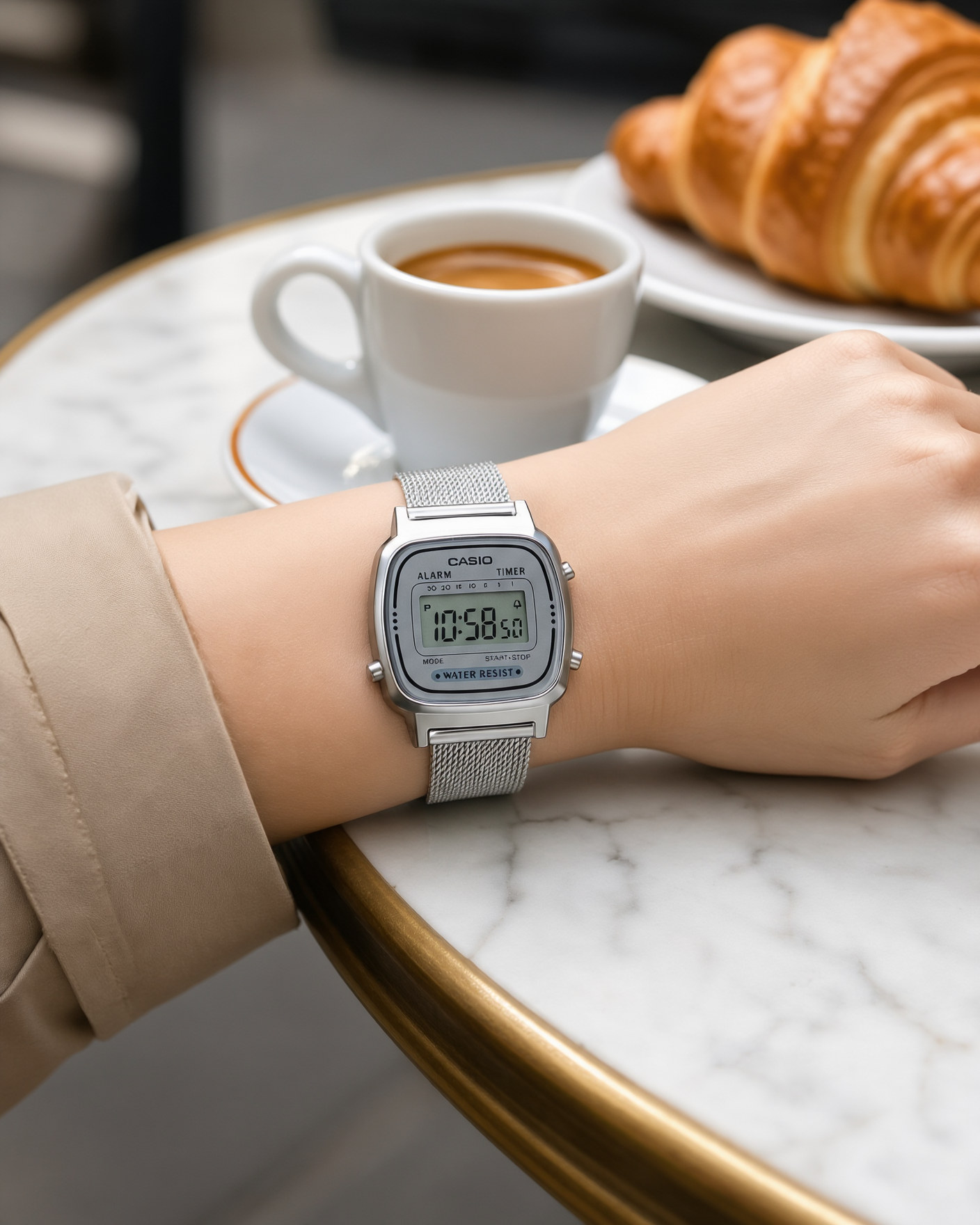 Casio Vintage LA670WEM-7EF silver Milanese mesh watch worn on a woman's wrist, on a marble café table with an espresso and a croissant