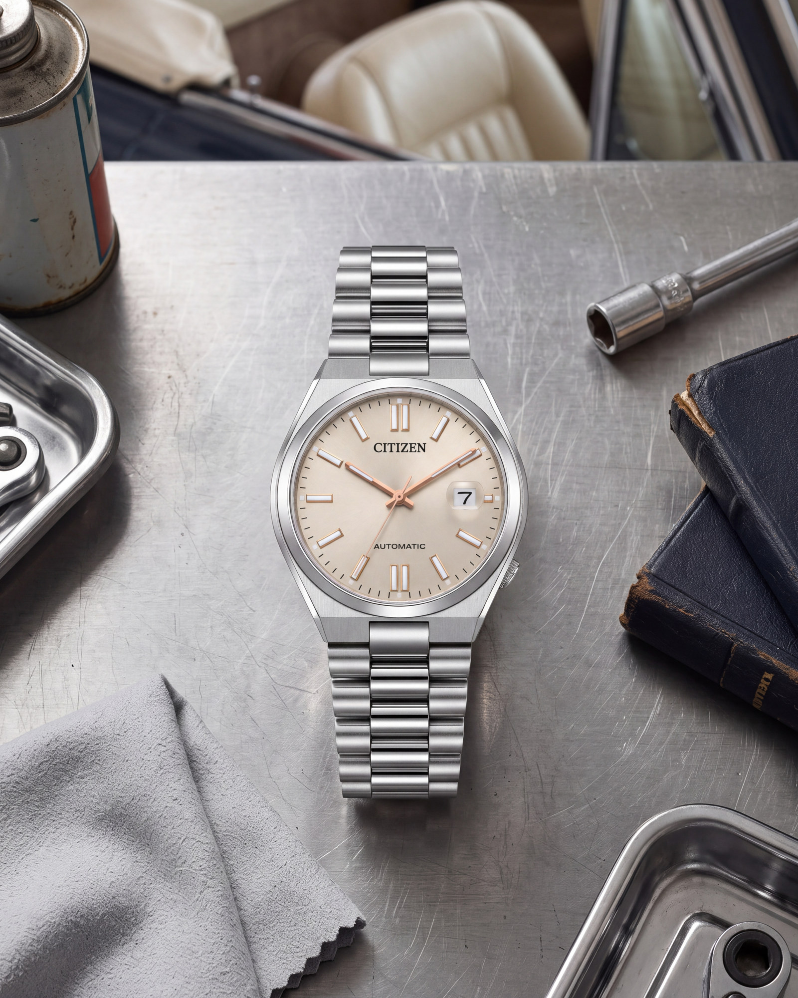 Montre Citizen Tsuyosa NJ0151-88W posée sur un établi métallique, avec cadran beige, bracelet en acier argenté et boucle déployante, entourée d'outils, de livres anciens et d'un chiffon gris.