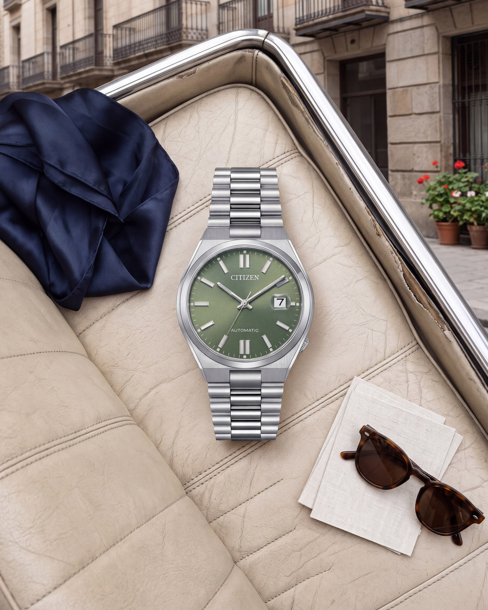 Montre Citizen Tsuyosa NJ0158-89Z posée sur une banquette en cuir, cadran vert, bracelet acier, boucle déployante, rue ancienne aux balcons en fer forgé.