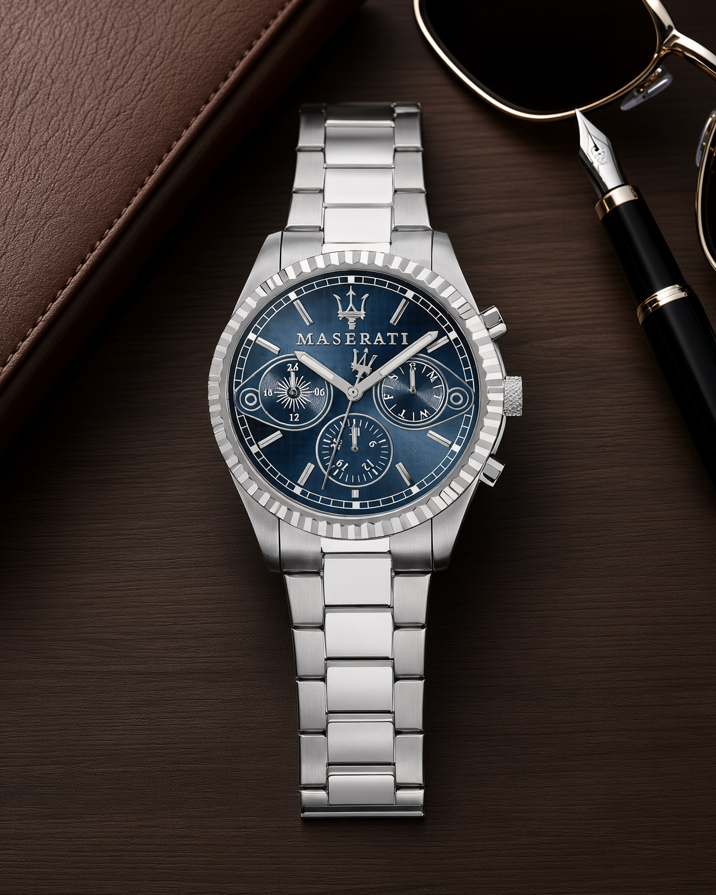 Maserati Competizione R8853100013 stainless steel watch with a blue dial, lying on a walnut desk next to a leather wallet, a fountain pen and sunglasses